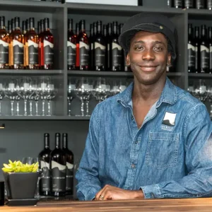 A young Black man smiling behind the counter of Los Milics wine bar.