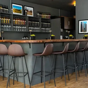 Los Milics wine tasting room bar with high stools and shelves of wine and glasses.