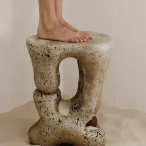 Open organic slumped sculptural clay form small with a figure standing on the seat or table top.