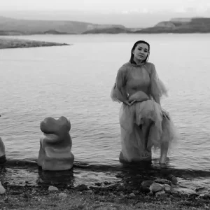 Four organic slumped clay sculptural forms on the edge of a lake with a young woman sitting on one.