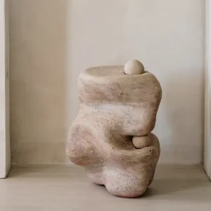 An organic slumped clay sculptural form with small clay balls with a smooth rock-worn like visual texture.